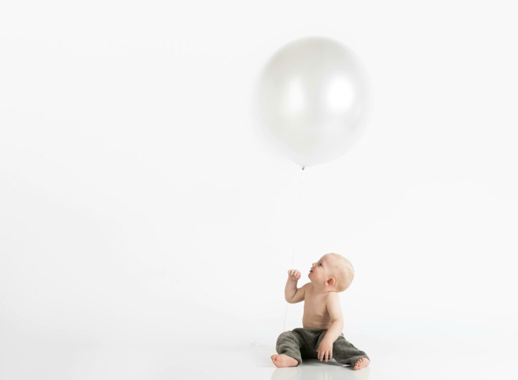Cute baby holding a large balloon in a bright studio setup, reflecting innocence and joy.