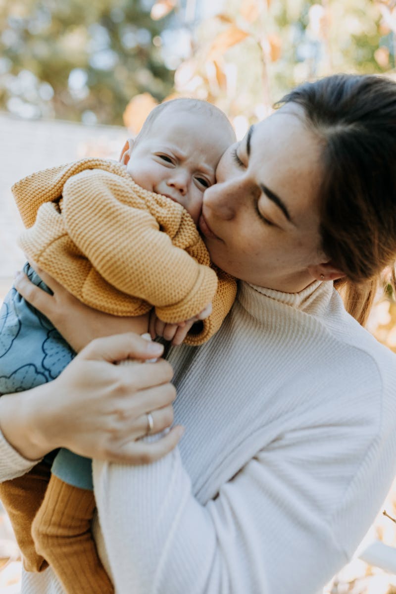 A tender moment captured as a mother lovingly embraces her baby outdoors in autumn.