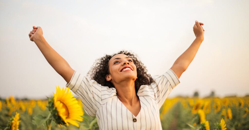 Joyful woman with arms raised in a sunflower field, embracing freedom and happiness.