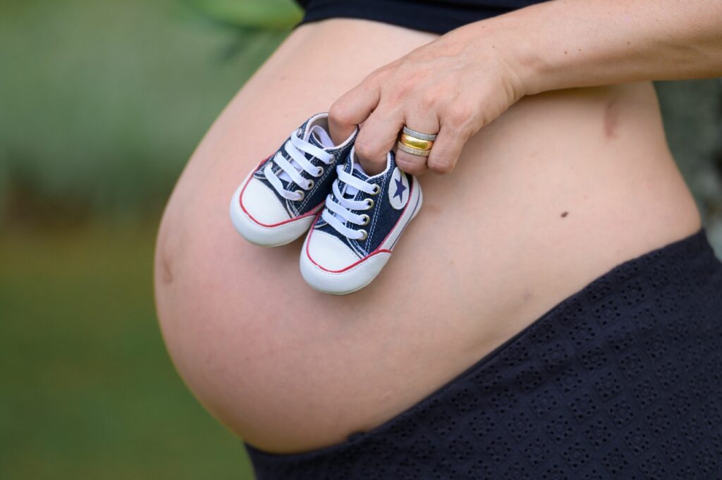 Close-up of a pregnant woman holding tiny sneakers on a baby bump.